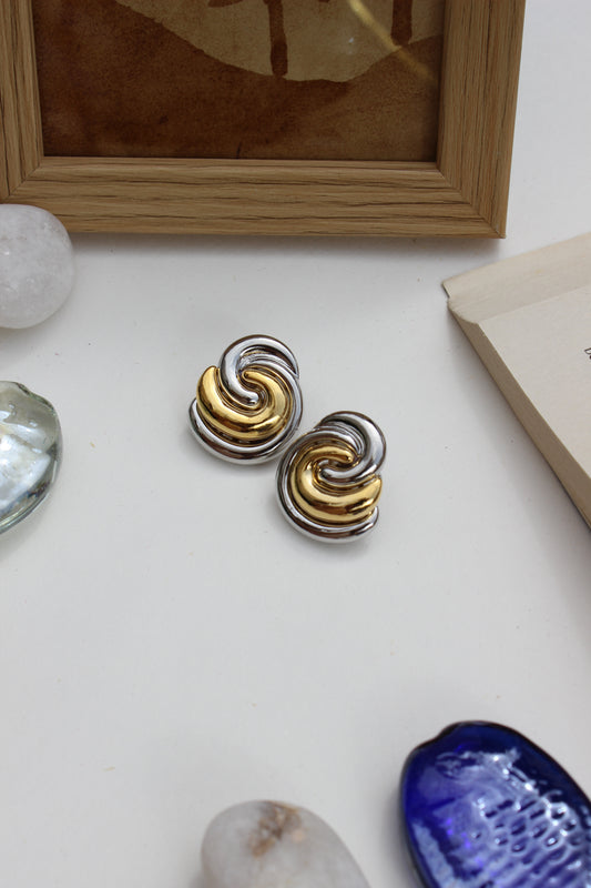 Gold and silver Yin-Yang stud earrings placed beside wooden photo frame and decorative shell