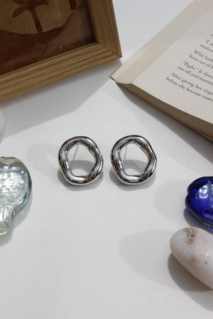 Lucid Frost Earrings on a textured surface with a book and seashell in the background