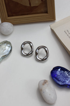 Lucid Frost Earrings on a white surface with a book, frame, and shell in the background