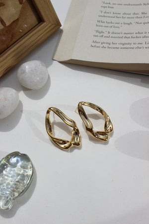 Golden Hug Earrings on a light surface with a book and decorative stones
