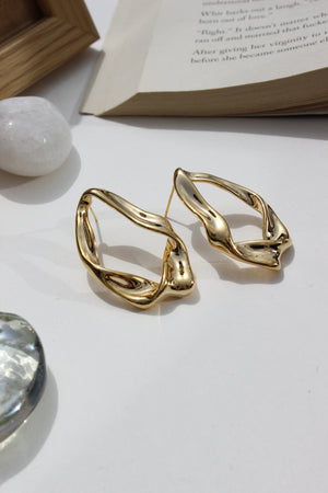 Golden Hug Earrings on a white surface with a blurred book and crystal in the background