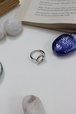 Lunar Trace Ring on a white surface with a blue seashell and book in the background
