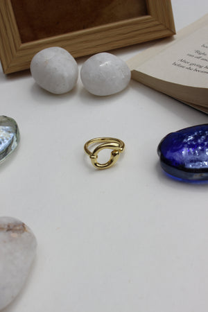 Decorative items including a Warm Loop Ring, blue glass seashell, and two white spherical stones on a light surface