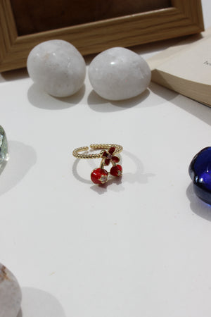 Close-up of a Kiss & Cherry Ring with red beads and gold chain on a white surface