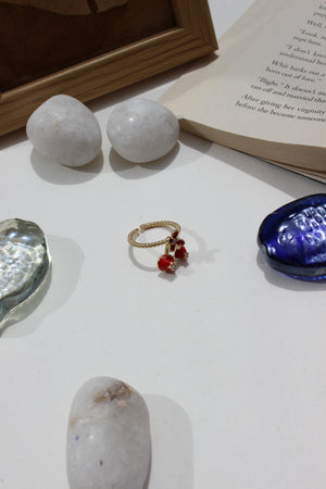 Kiss & Cherry Ring on a white surface with stones and an open book