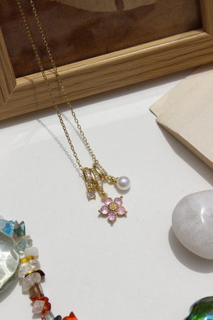 Jewelry including a Twinkle Flora Charms Pendant Necklace on a light surface with a wooden frame