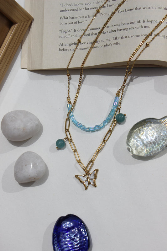 Butterbead Layered Necklace on a white surface with stones and an open book