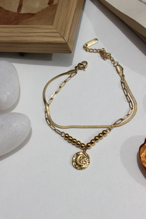 Golden Phase Layered Bracelet on a light surface with a wooden frame and stones in the background