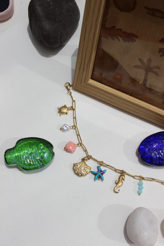 Oricca Charms Bracelet on a white surface with decorative seashell