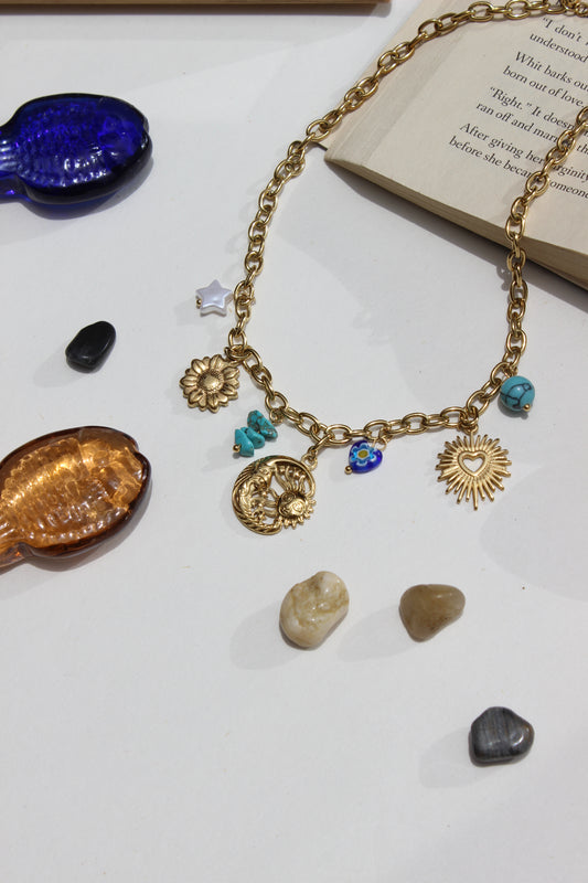 Solaris & Selene Charms Necklace with charms on a white surface with seashells and a book