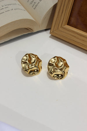 Musecore Stud Earrings on a white surface with an open book in the background