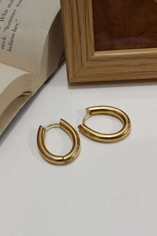 Aurume Earrings on a white surface with a wooden frame and book corner in the background