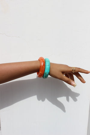 Hand wearing colorful Peach Orbit Bangle Bracelets on a white background