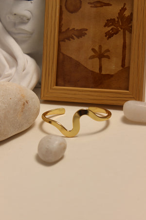 Magic Wave Cuff Bracelet on a beige wall with a framed picture and stones below