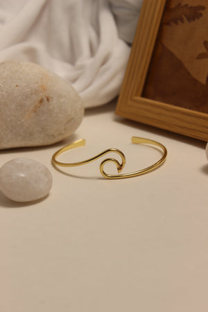 Maree Cuff Bracelet on a neutral background with stones and a framed picture