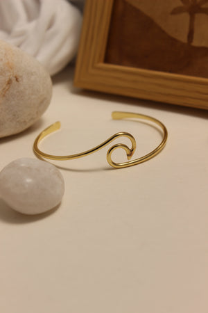 Maree Cuff Bracelet on a textured surface with pebbles and a wooden frame in the background