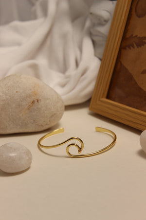 Maree Cuff Bracelet on a white surface with stones and a wooden frame in the background
