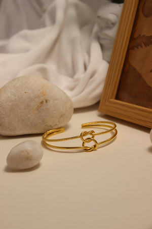 Eterna Knot Cuff Bracelet on a stone with a wooden box in the background