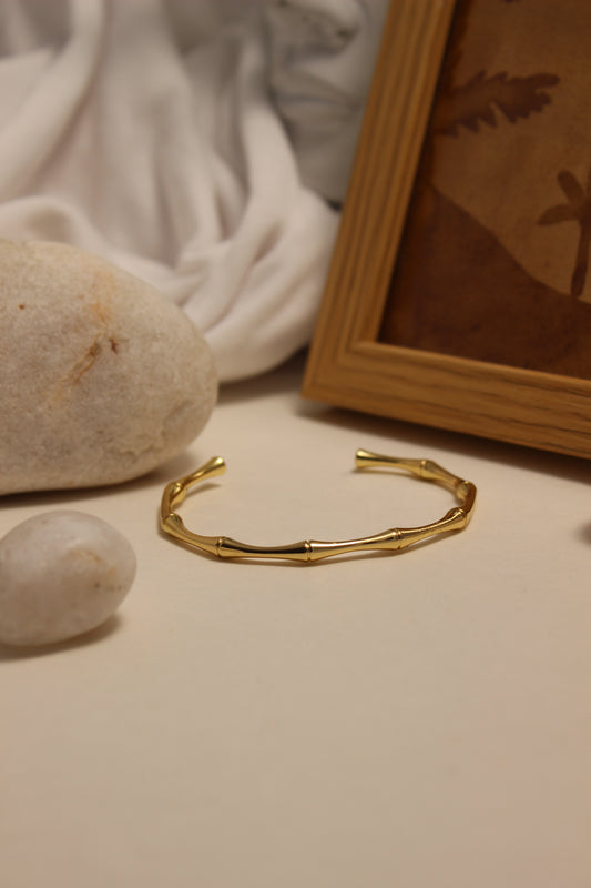 Golden Reed Cuff Bracelet on a stone surface with a blurred background