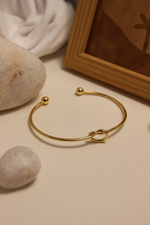 Entwine Cuff Bracelet on a surface with stones and a wooden frame in the background