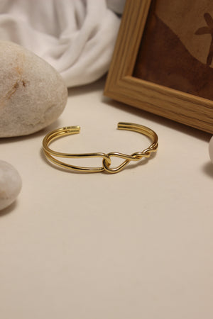 Aurum Dualis Cuff Bracelet on a neutral background with stones and fabric