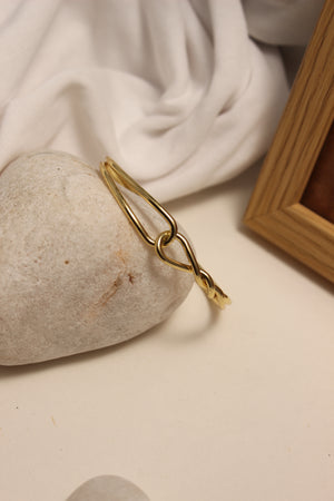 Aurum Dualis Cuff Bracelet on a stone with a soft fabric background