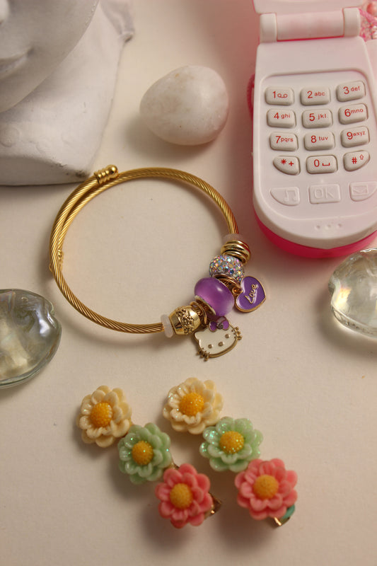 Violet Purr Bracelet with decorative charms on a light surface with a toy phone and stones
