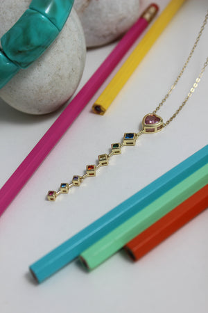 Rose Descent Necklace with gemstones on a white surface with colorful pencils