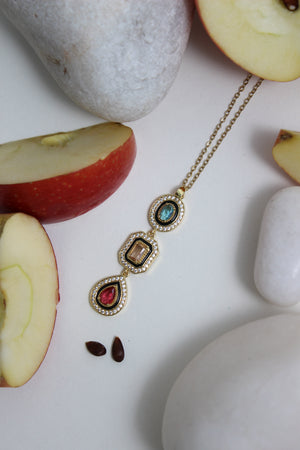 Noir Royale Necklace with colored stones on a white surface with sliced apples and stones