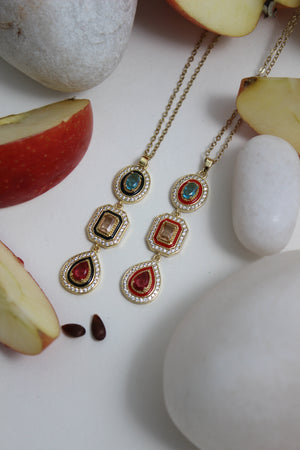 Noir Royale Necklace with gemstones on a white surface with apples and stones