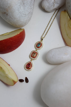 Empress Flame Necklace with gemstones on a white surface with apples and stones