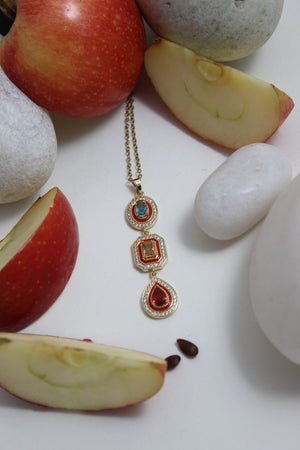 Empress Flame Necklace with red and blue stones on a white surface with apples and stones