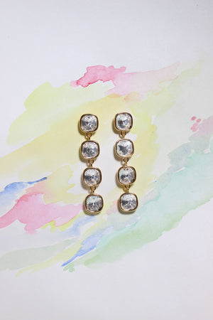 Pair of Glacier Glow Earrings with clear stones on a colorful watercolor background