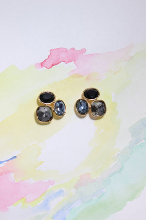 Pair of Blue Mirage Earrings with black gemstones on a colorful watercolor background