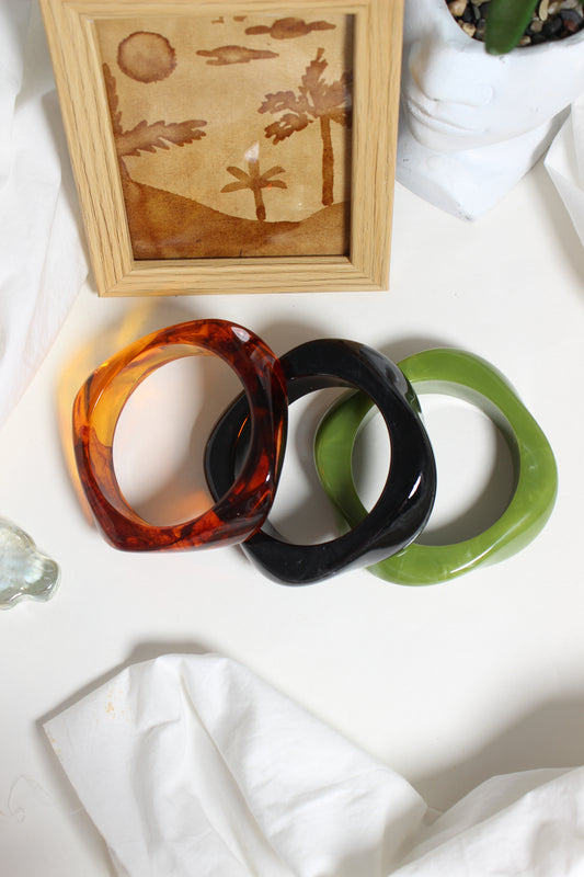 Aurora Stacks Resin Bangles on a white surface with a wooden frame and plant in the background