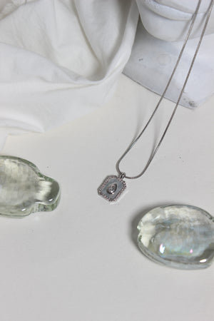 Emeraude Glow Pendant Necklace on a white fabric background