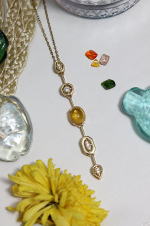 Coralie Necklace on a white surface with a yellow flower and green gemstone