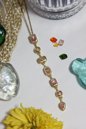 Blush Pastel Pour Necklace on a white surface with decorative flowers