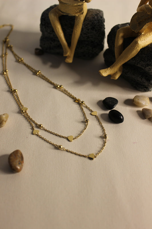 LoveDots Layered Necklace on a surface with rocks and a gold figurine