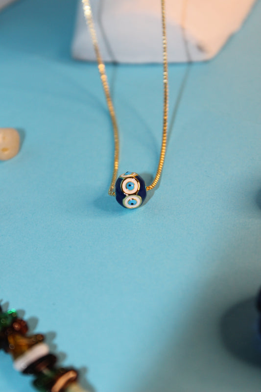 Close-up of a decorative glass bead on a Evil Eye Gem Pendant Necklace against a blue background