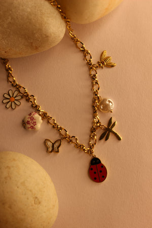 Bloom Folk Charms Necklace on a pink surface with stones