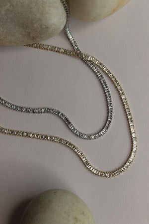 Twilite Necklace on a light pink surface with stones