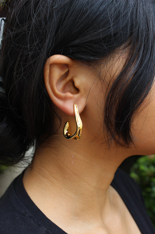 Spinelle Half Hoop Earrings worn by a model with dark hair, against a blurred natural background.
