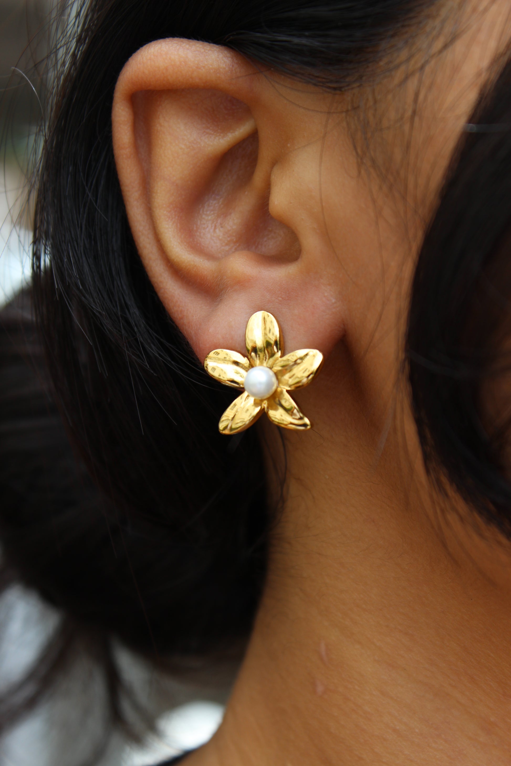 Golden Whisper Stud Earrings on model's ear with blurred background