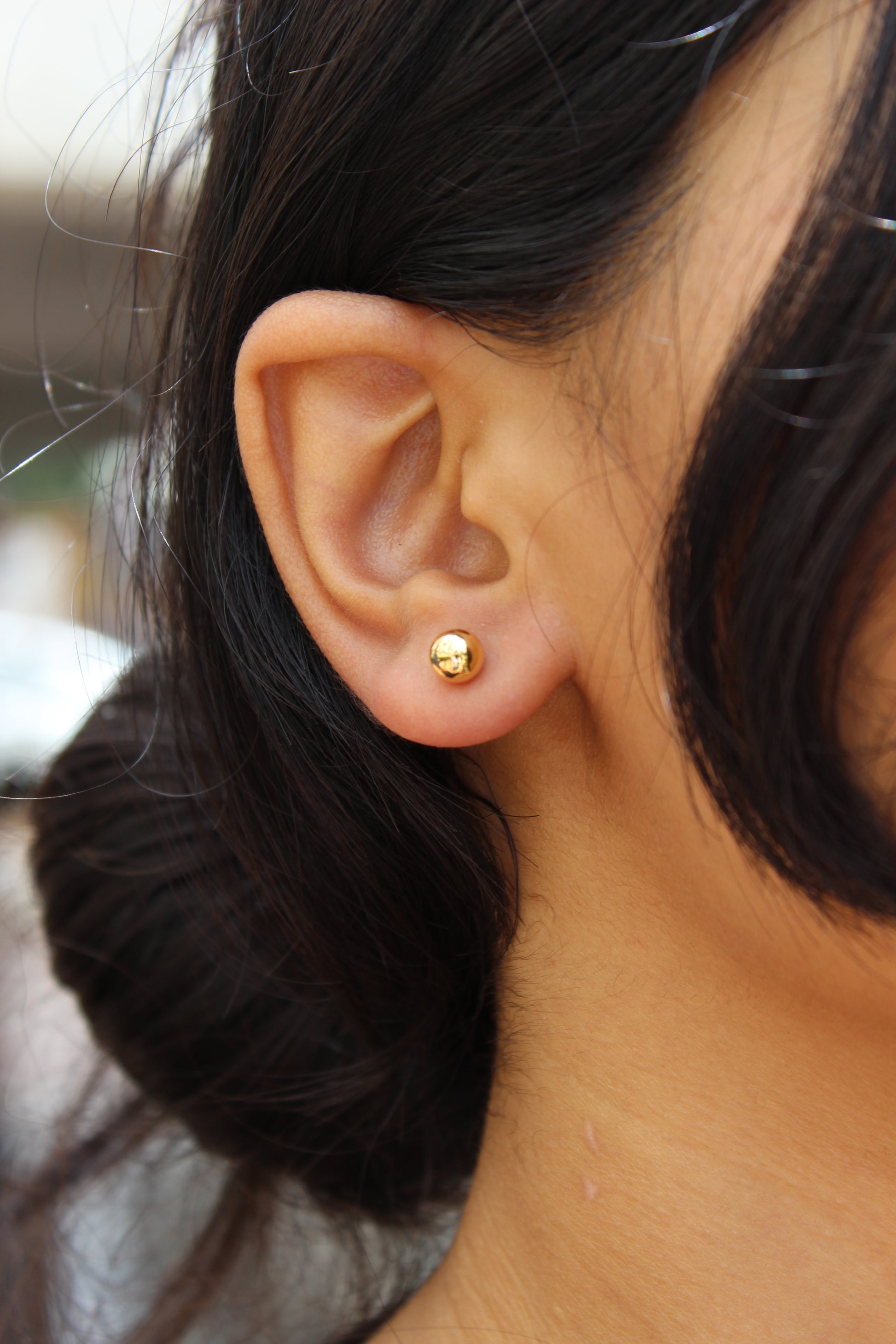 Close-up of an ear wearing a gold Velisse Stud Earrings with blurred background