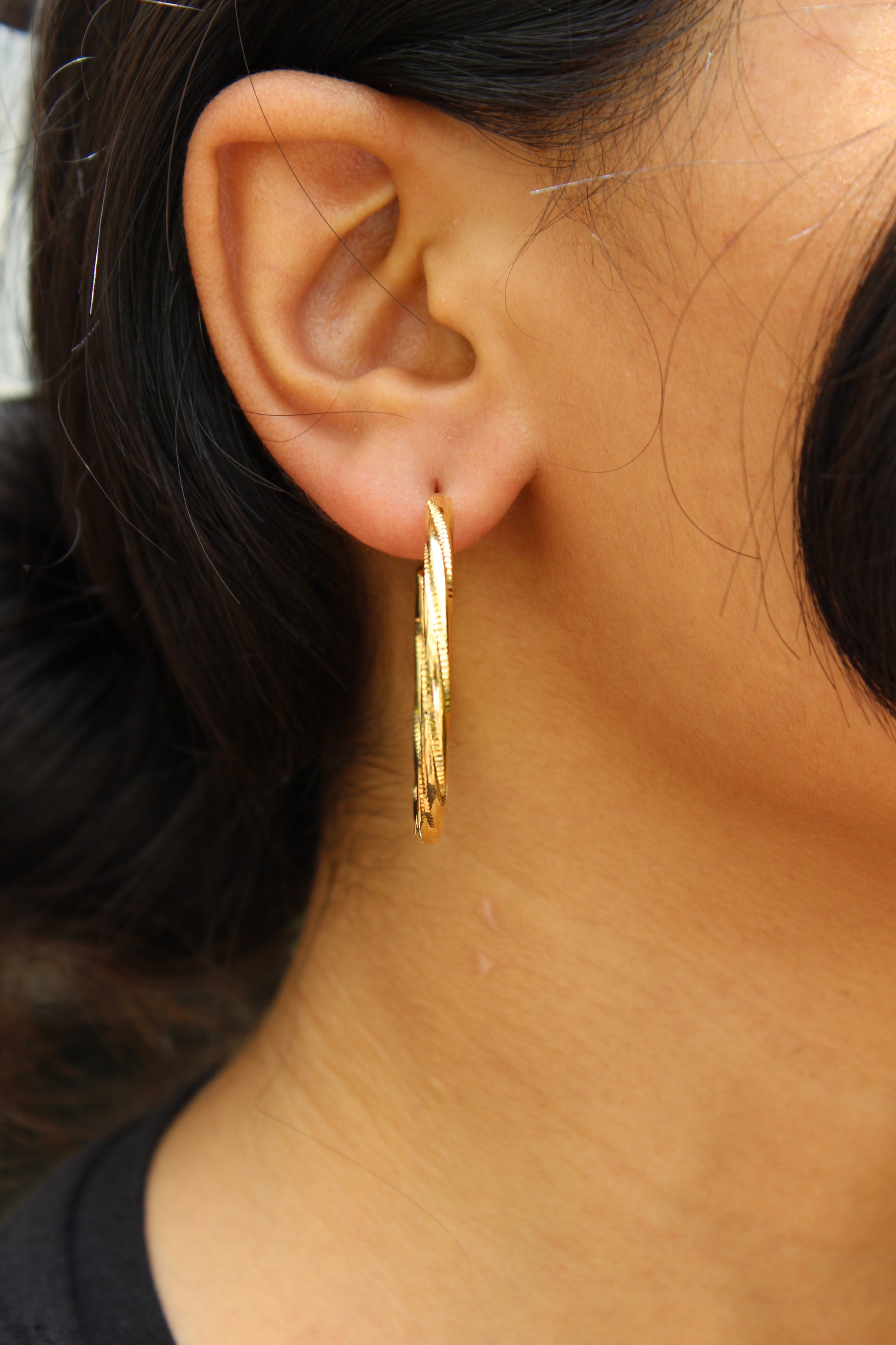 Close-up of a model wearing gold Twistline hoop earrings