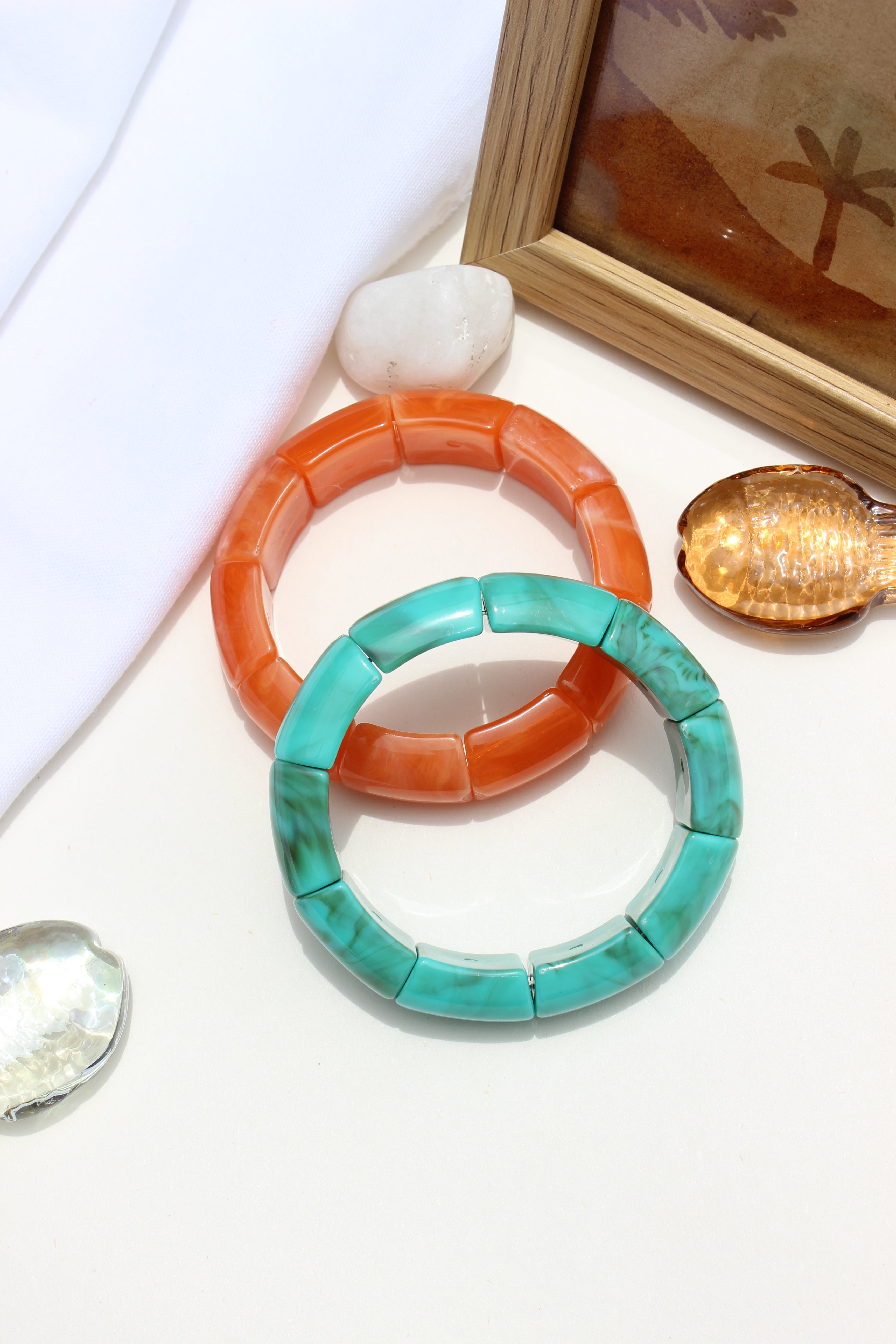 Peach Orbit Bangle Bracelets on a white surface with a wooden frame and seashells in the background