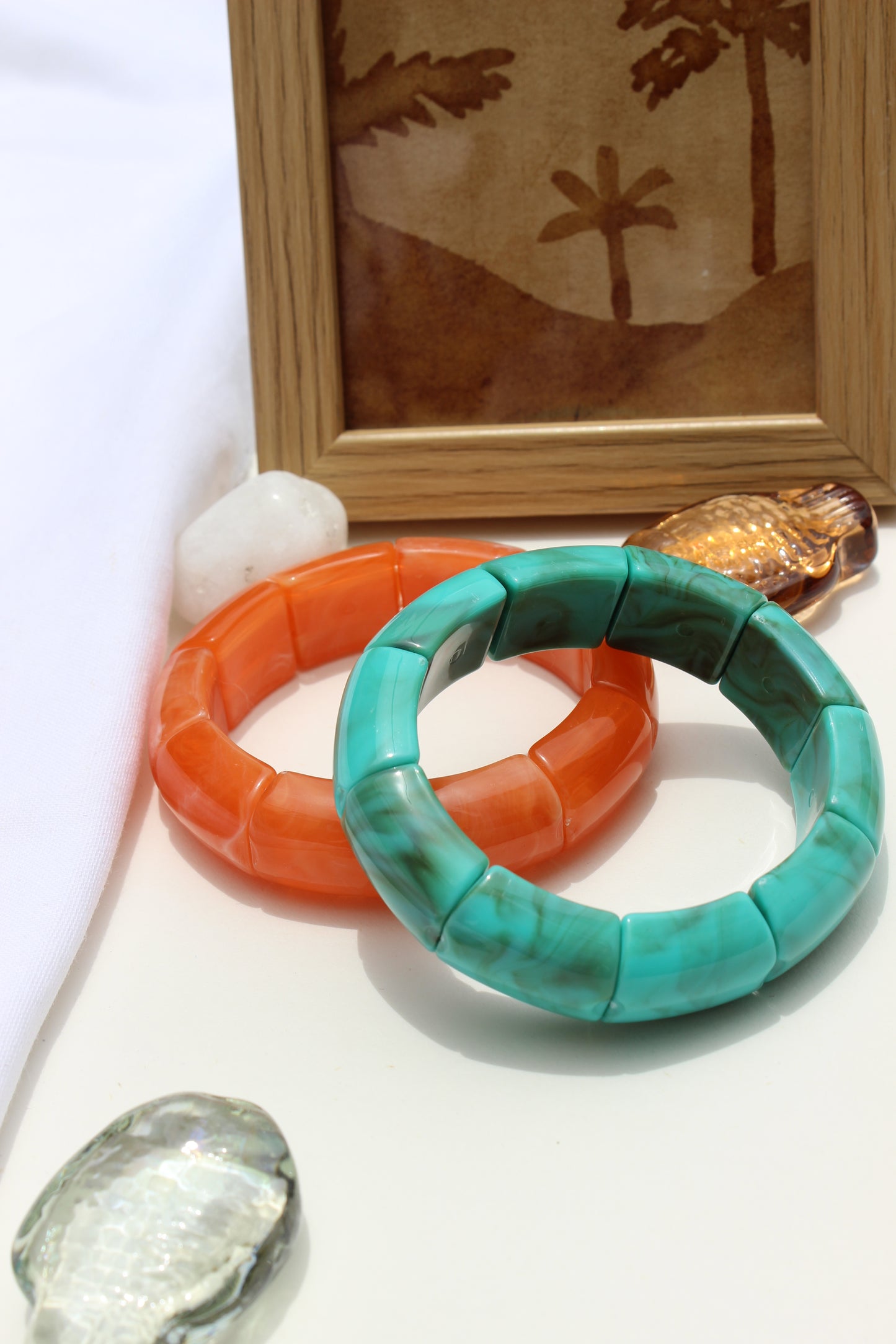 Peach Orbit Bangle Bracelets on a white surface with a wooden frame and decorative stones in the background