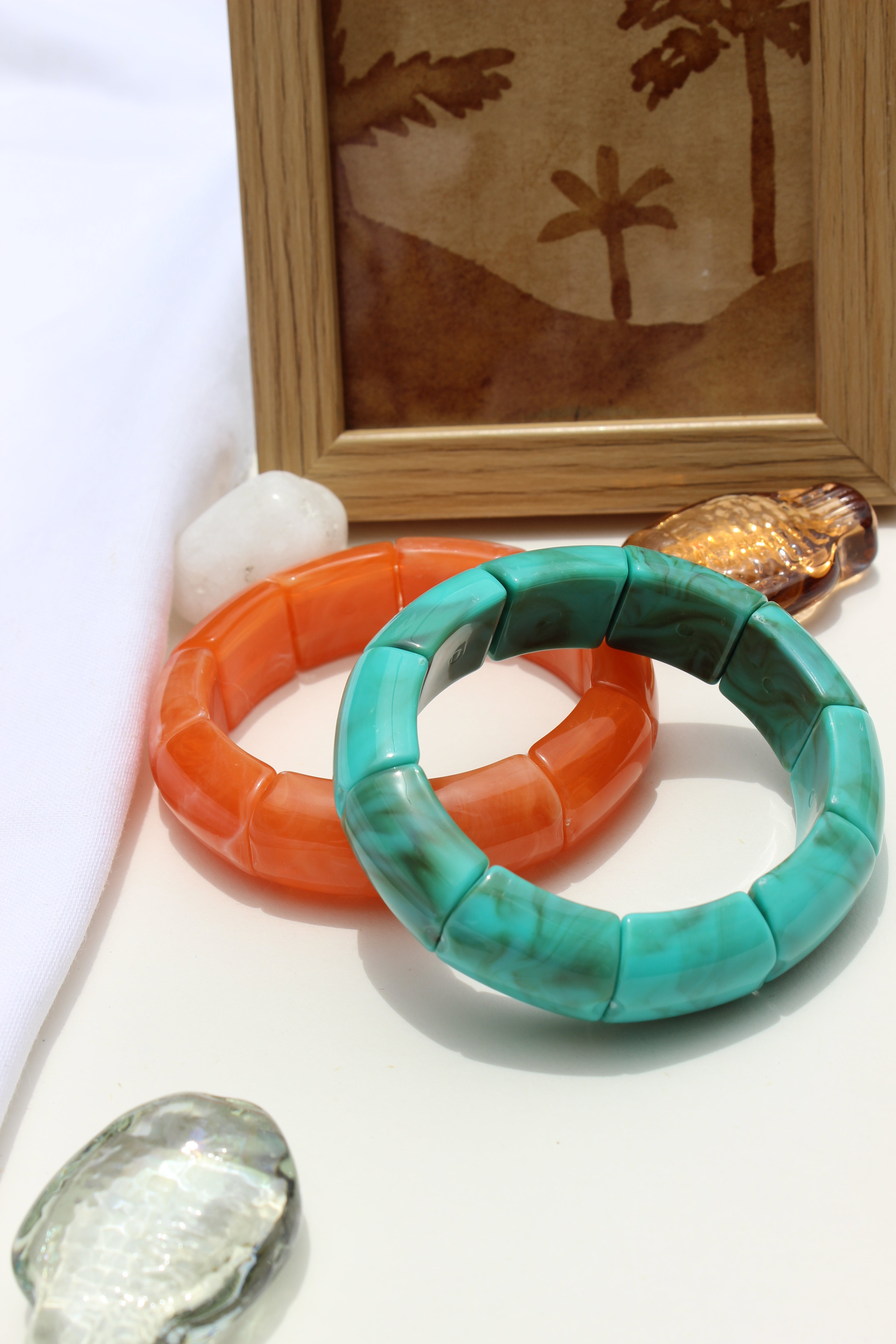 Peach Orbit Bangle Bracelets on a white surface with a wooden frame and decorative stones in the background