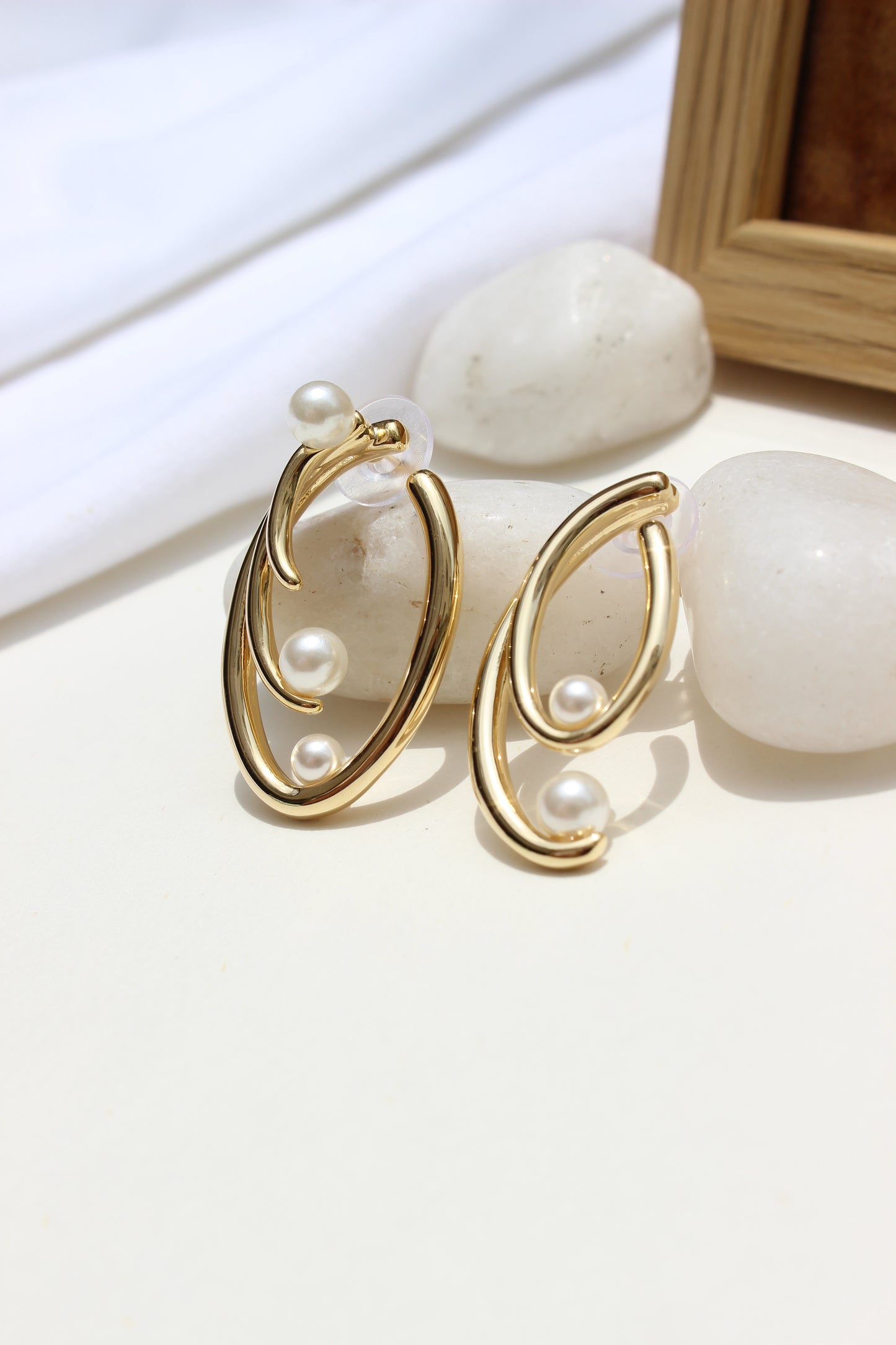 Not quite Twins Earrings on a white surface with stones and wooden frame